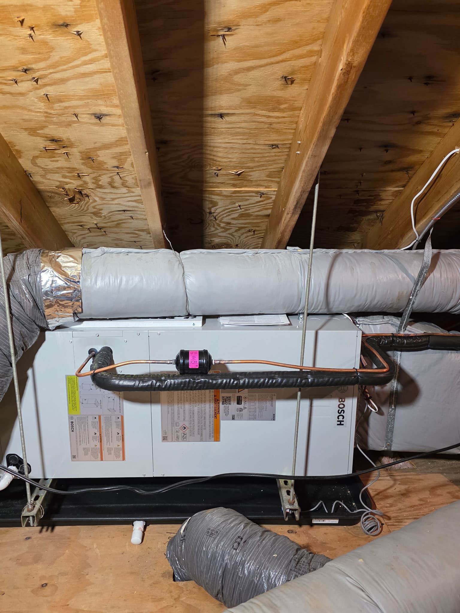 Bosch HVAC unit installed in an attic with insulated ductwork and copper refrigerant lines.