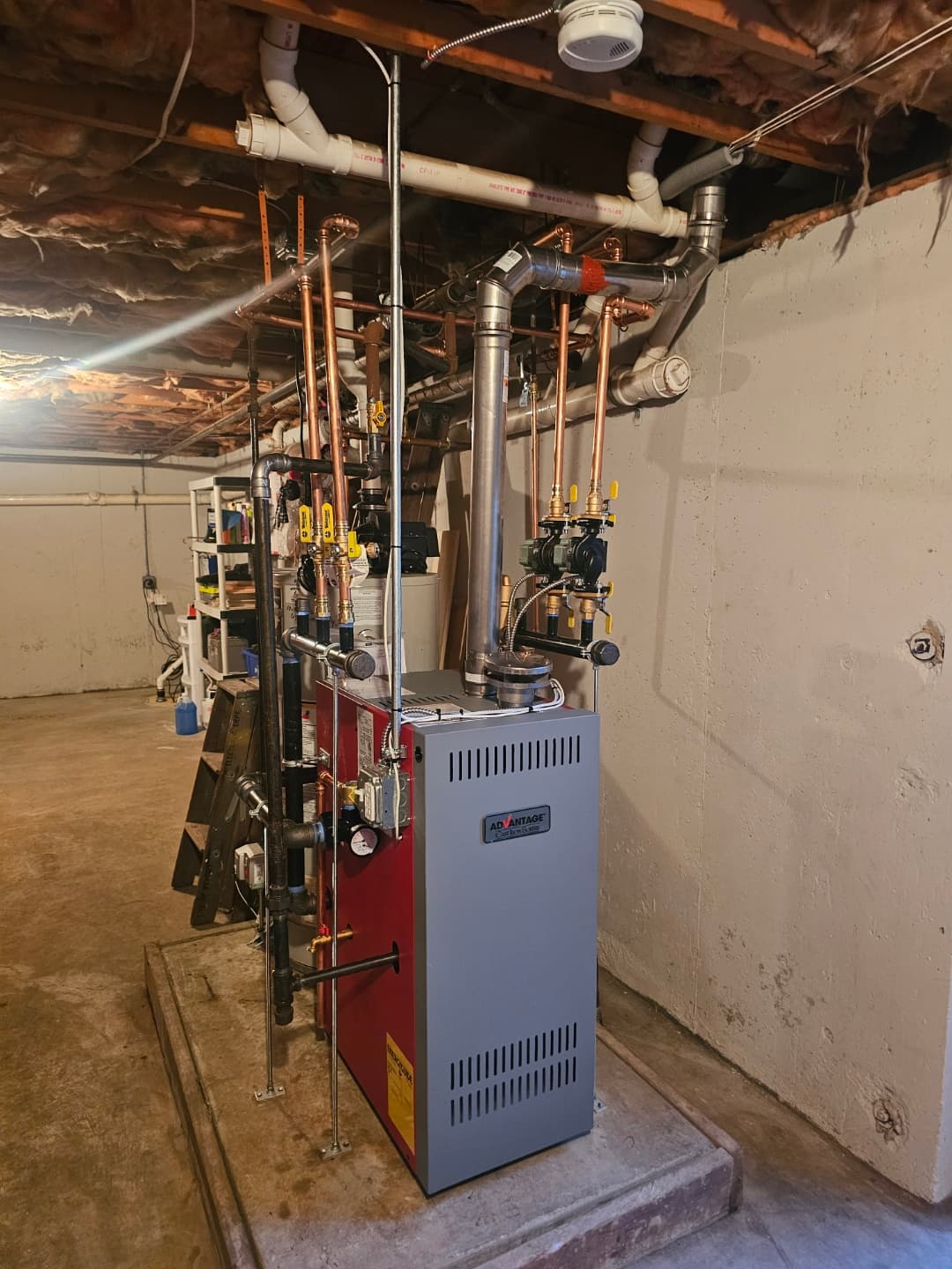 Red and grey Advantage boiler system with complex copper piping in an unfinished basement.